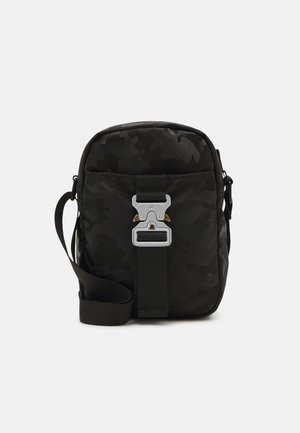 Svart kamouflage crossbody-väska med en strukturerad yta, utrustad med en silverfärgad metallspänne, justerbar rem och rektangulär form.