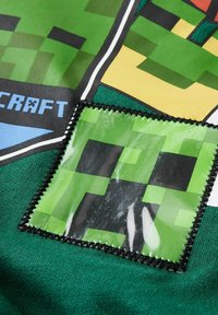 Sweat-shirt vert avec un design de creeper pixelisé. La texture est douce, avec un patch en plastique brillant mettant en valeur les détails. Accents de couture noire.