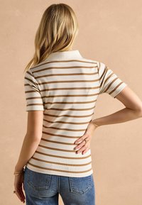 Pruhovaná polo tričko v krémovej a hnedej farbe, s krátkymi rukávmi, s priliehavým strihom a ribbum textúrou. Má klasický golier a minimálne detaily.