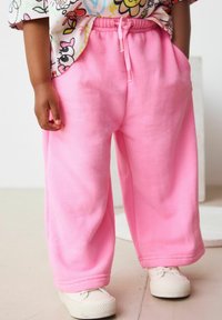 Rosa sweatpants med elastisk talje og snoretræk. Blødt stof, bred bendesign og sidelommer. Sammen med hvide sneakers.