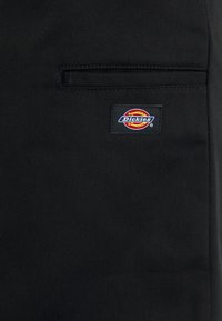 Black fabric with a slight texture, featuring a rear pocket and a colorful Dickies logo label sewn onto the fabric.