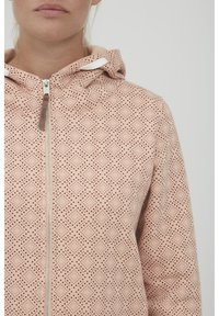 Felpa leggera rosa con cerniera, caratterizzata da un motivo testurizzato di piccoli punti e diamanti. Presenta un cappuccio con lacci e dettagli con cerniera argentata.