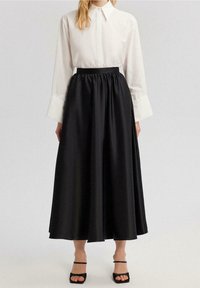 Falda de satén negra con cintura fruncida. Combinada con una camisa blanca de botones con puños anchos. Sandalias negras de tiras completan el look.