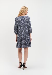 Granatowa sukienka w kwiaty z rękawami o długości trzech czwartych, warstwowym dołem i miękkiego materiału. Para czarnych sandałów na obcasie dopełnia całość.