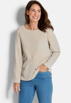Lichtbeige langemouwen top met een ronde halslijn, gemaakt van een gestructureerde stof. Gecombineerd met blauwe jeans, wat zorgt voor een ontspannen pasvorm.