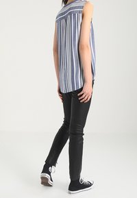 Top sin mangas en azul y blanco a rayas con corte holgado, combinado con pantalones ajustados negros y zapatillas negras, visto desde atrás.