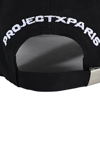 Gorra negra de tela con el texto bordado en blanco "PROJECTXPARIS" en la parte trasera, que cuenta con un clip de ajuste metálico para el tamaño.