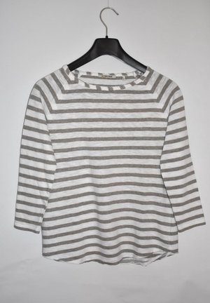 Chemise à manches longues à rayures horizontales grises et blanches suspendue à un cintre en plastique noir sur un fond blanc.