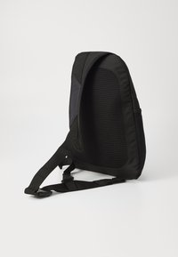 Mochila preta com um painel traseiro em malha texturizada, alça ajustável e forma elegante e afunilada. Apresenta um fecho e um design minimalista.