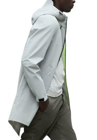 Chaqueta impermeable de color gris claro con capucha, que presenta un cierre de cremallera y un interior de un verde brillante. Tiene bolsillos laterales y un corte relajado.