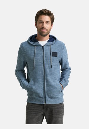 Niebieska, w poziome paski, bluza rozpinana z kapturkiem, z granatowym wnętrzem, przednimi kieszeniami, sznurkiem do ściągania kaptura oraz małą czarną naszywką na klatce piersiowej.