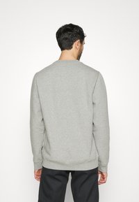 Felpa grigia con scollo rotondo, maniche lunghe, polsini e orlo a costine, caratterizzata da una texture liscia e un design minimalista.