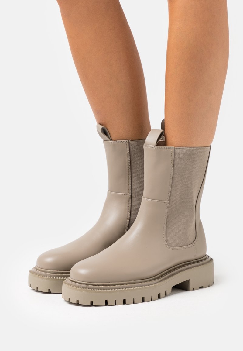 Bottes courtes beiges en cuir lisse avec des panneaux latéraux élastiques, une semelle en caoutchouc texturée et des languettes pour faciliter l'enfilage.