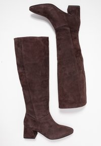 Botas de ante marrón hasta la rodilla con punta cuadrada y un tacón grueso. Textura suave con un diseño de caña ajustada.