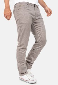 Lichtgrijze geweven katoenen broek met een gestructureerde afwerking, tapered fit en subtiele zakdetails, gecombineerd met witte sneakers.