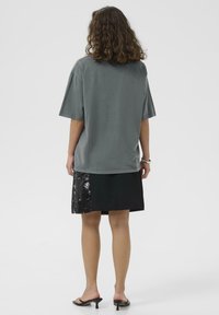 Grå oversized t-shirt med korte ærmer, parret med en sort nederdel med palietter på venstre side. Enkel, afslappet design.