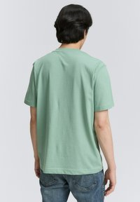 Tricou din bumbac de culoare verde mentă, cu mâneci scurte, gât rotund și o croială lejeră, asortat cu blugi din denim albastru.