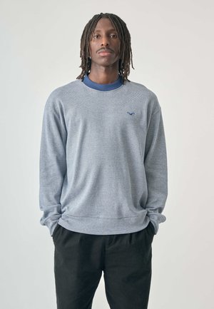Grauer langärmeliger Sweatshirt mit gestreiftem Muster, geripptem Ausschnitt und Bündchen, mit kleinem Logo auf der Brust, kombiniert mit schwarzen Hosen.