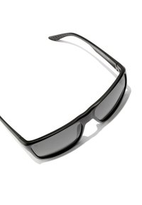 Ochelari de soare negri cu lentile gri, design elegant și brațe texturate negre. Ramele au un aspect ușor, sportiv.