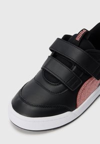 Baskets noires avec une bande en paillettes roses, semelle blanche, deux bandes Velcro et logo "Puma" sur le tirant en tissu noir.