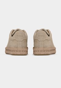 Ζευγάρι μπεζ αθλητικά παπούτσια από υφαντό ύφασμα με μεσαία σόλα υφής σχοινιού, εμφανιζόμενα από πίσω, σε λευκό φόντο.