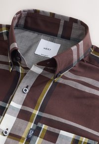 Camicia a quadri marrone con accenti gialli, grigi e bianchi. Colletto con bottoni, vestibilità regolare, etichetta visibile. Tessuto di cotone con texture liscia.