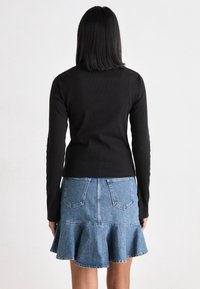 Zwarte longsleeve gecombineerd met een lichtblauwe denim rok met een uitlopende zoom en achterzakken, gezien van achteren.