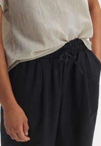 Helles graues, geripptes Oberteil kombiniert mit schwarzen, locker sitzenden Hosen mit elastischem Bund und Kordelzug, sichtbaren Taschen und glatter Textur.