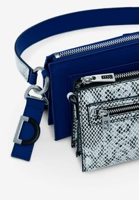 Blå lædertaske med sølvhardware, prydet med en tekstureret sort-hvid mønstret pouch og en aftagelig bæltestil skulderrem. Lynlåslommer.