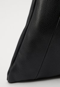 Black leather handbag featuring a textured surface, angular design, and structured shape. Notable seams enhance its contemporary look.