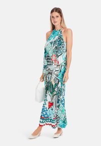 Halter neck maxi dress in a vibrant blue, green, red, and white print; features floral and geometric patterns, paired with a white handbag.