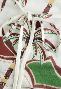Gros plan sur un tissu blanc avec un motif floral géométrique coloré et une cordelette blanche nouée en un nœud.