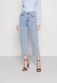 Světle modré tričko s dlouhým rukávem je zkombinováno s vysokými, světle modrými džíny s rovnými nohavicemi. Černé sandály na podpatku podtrhují outfit.