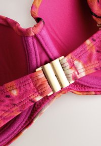 Gros plan d'un soutien-gorge à motifs roses et oranges avec des bonnets rembourrés et une fermeture métallique dorée au centre devant.
