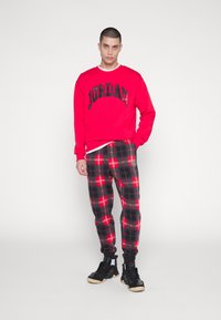 Röd sweatshirt med texten "JORDAN"; svarta och röda rutiga joggingbyxor; svarta sneakers. Slät tyg; avslappnad passform.