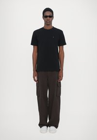 Tricou negru din bumbac cu mâneci scurte și un mic emblemă, combinat cu pantaloni cargo maro, având buzunare laterale și adidași albi.