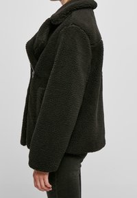 Sort fleecejakke med krave, struktureret overflade og sidelommer. Løs pasform med lynlåslukning og vide ærmer.