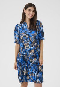 Korte mouwen blauwe bloemenjurk met een geplooide rok. Heeft een v-hals en kleurrijke bloemenpatronen in tinten blauw en bruin.