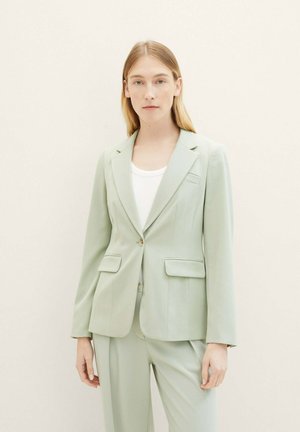 Lichtgroen kostuum met een op maat gemaakte blazer met twee voorzakken, notchrevers en een enkele knoopsluiting, gecombineerd met bijpassende broeken.
