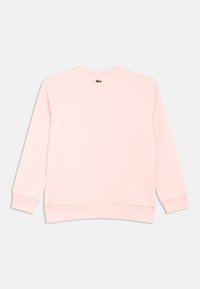 Sweatshirt rosa claro com gola redonda e mangas compridas. Apresenta punhos e bainha canelados, pequeno logótipo verde nas costas perto do pescoço.