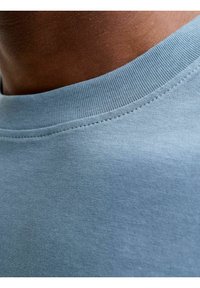 Jasnoniebieska bawełniana koszulka z okrągłym dekoltem. Tekstura materiału jest gładka, a wykończenie szwów szczegółowe wzdłuż krawędzi kołnierza.