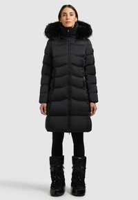 Svart vadderad jacka med fuskpäls runt huvan, dragkedja framtill och sidofickor; kombinerad med svarta isolerade stövlar.