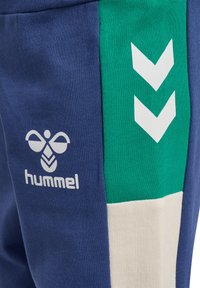 Marineblauwe sweatpants met een groen accentpaneel, witte chevronpatronen en een logo. Gemaakt van zachte stof met een gestructureerde afwerking.