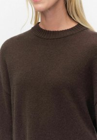 Donkerbruine gebreide trui met een geribbelde ronde halslijn en een zachte textuur, met een relaxte pasvorm en zonder zichtbare patronen of hardwaredetails.