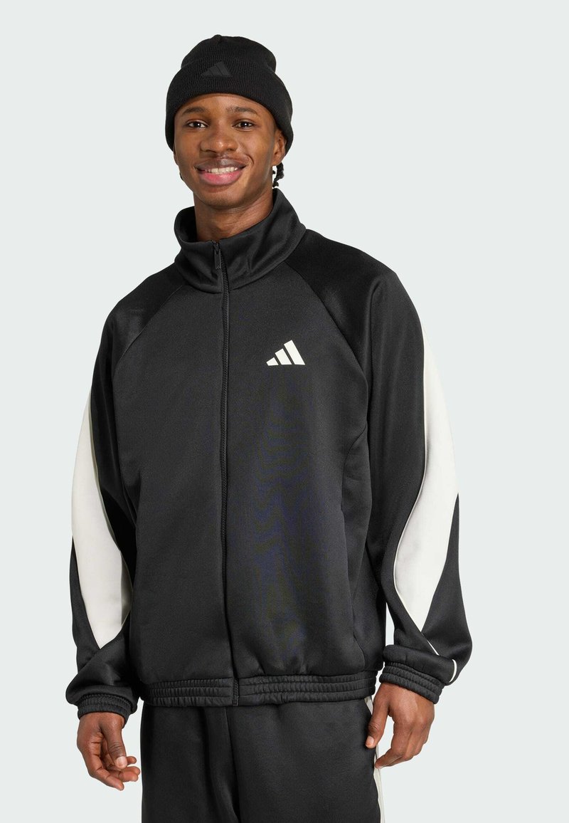 Fato preto com fecho éclair e detalhes brancos, feito de um tecido suave. Apresenta um colarinho alto e punhos em malha, combinado com um gorro preto.