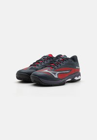 Buty sportowe w kolorze ciemnoszarym z czerwonymi akcentami, z fakturowanym wzorem, wyściełanym kołnierzem oraz solidną czarną podeszwą z falistym wzorem.