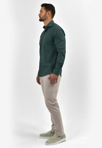 Donkergroene overhemd met knopen, lichtbeige broek en lichtgroene instappers. Glad materiaal, slim fit en minimalistisch ontwerp.