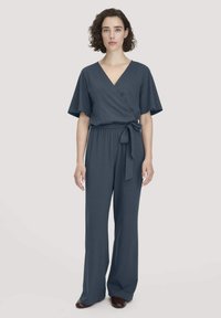 Grauer Wickel-Jumpsuit mit V-Ausschnitt, kurzen Ärmeln, weitem Bein und einem passenden Gürtel in der Taille. Aus weichem, fallendem Stoff gefertigt.