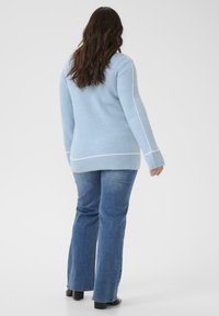 Pull tricoté bleu clair avec bandes blanches sur les côtés, col rond et manches longues. Assorti à un jean évasé bleu foncé et des chaussures noires.