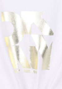 Camiseta blanca con un gráfico en texto metálico dorado en negrita y flechas. El texto incluye "NY EST. 1989" con una textura suave y brillante.